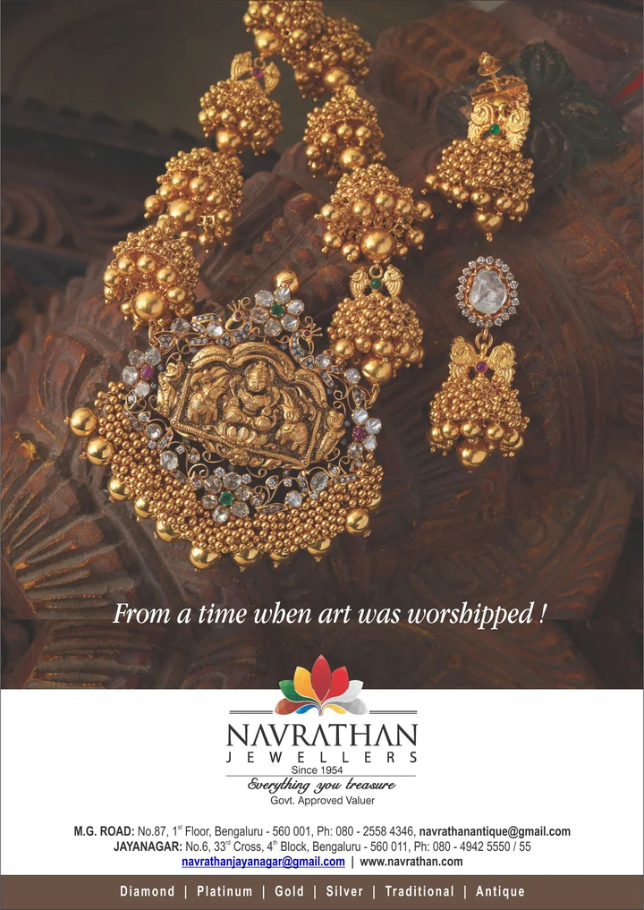 An ornate gold necklace and earrings photographed on carved wood